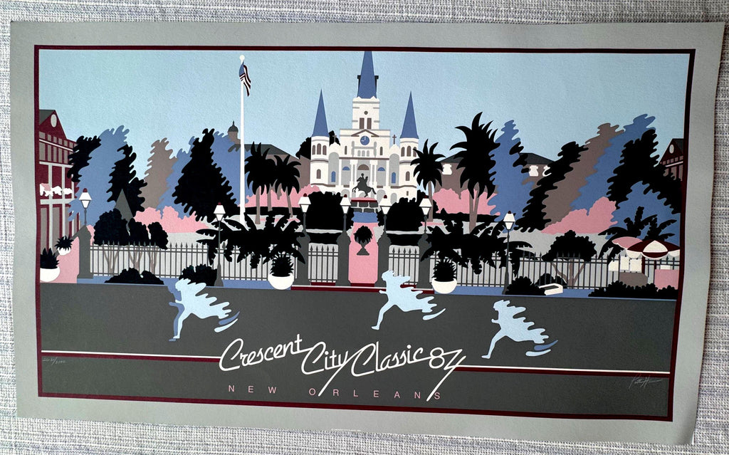 May include: A vintage print of the Crescent City Classic '87 in New Orleans. The artwork features a cityscape with a cathedral, palm trees, and runners. The color palette includes blue, pink, gray, and black.