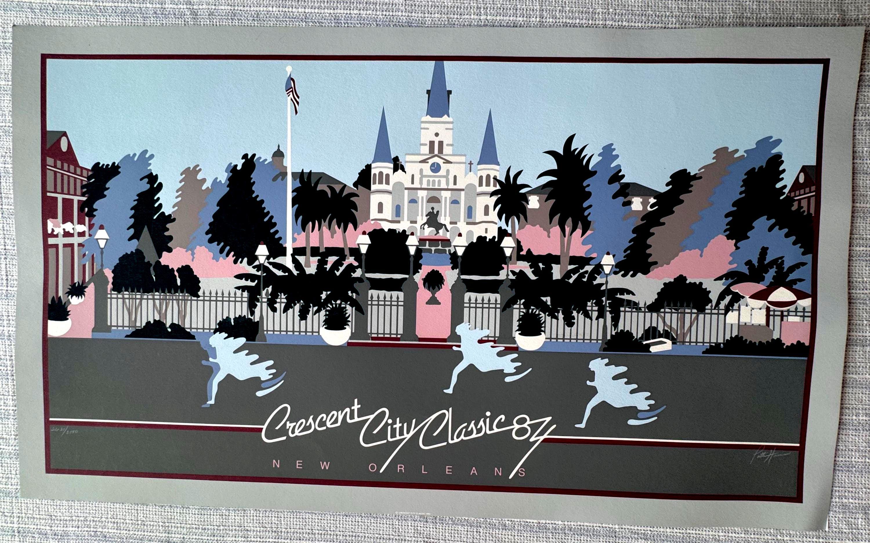 May include: A vintage print of the Crescent City Classic '87 in New Orleans. The artwork features a cityscape with a cathedral, palm trees, and runners. The color palette includes blue, pink, gray, and black.
