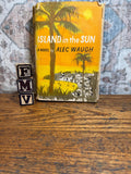May include: A vintage book titled "ISLAND in the SUN" by Alec Waugh, featuring a yellow cover with a palm tree illustration. The book is set on a wooden surface, with wooden letter blocks spelling "FMV" in the foreground.