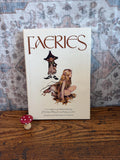 May include: A hardcover book titled Faeries, described and illustrated by Brian Froud and Alan Lee, featuring a central illustration of a small creature and a winged figure. A small red and white spotted mushroom figurine sits to the left.