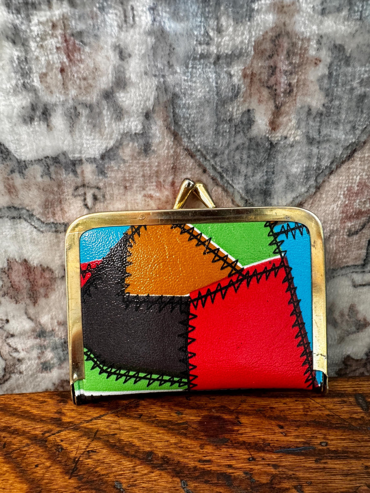 May include: A rectangular coin purse featuring a multi-colored patchwork design in red, orange, green, black, and blue. The purse has a gold-toned metal frame with a kiss-lock closure and visible black zigzag stitching along the seams.