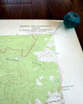 May include: A topographic map titled Browns Cove Quadrangle Virginia 7.5 Minute Series with green contour lines and text, accompanied by a small, round, teal-colored glass marble resting on the upper right corner of the paper document.