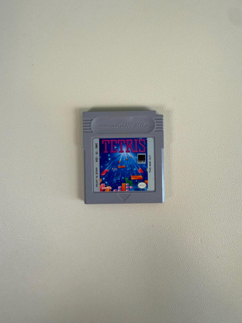 May include: A gray Nintendo Game Boy video game cartridge for Tetris. The label features the word TETRIS in large purple letters above a blue background with falling geometric blocks. Text on the label includes DMG-TR-USA and MADE IN JAPAN.